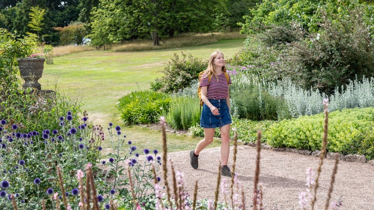 Visitor walking along a gravel path that's running through the middle of a garden full of flowers and green bushes at Killerton, Devon